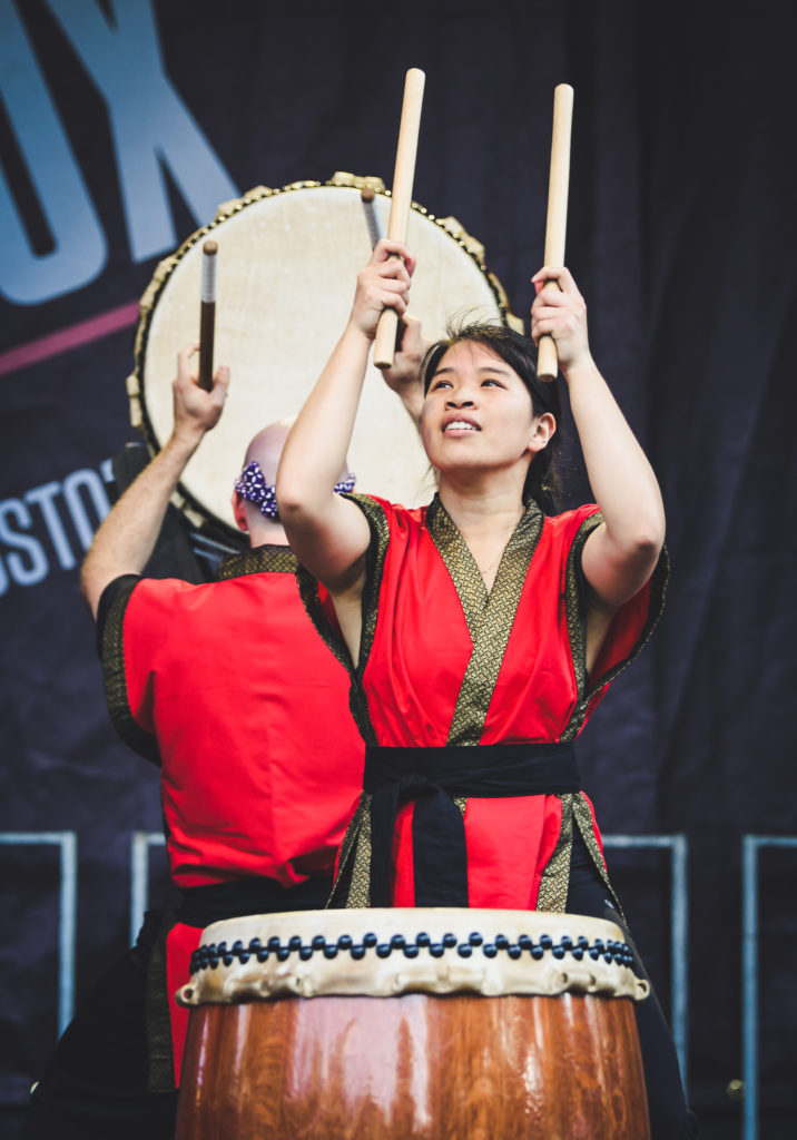 Two drummers dressed in traditional Japanese clothing play Japanese drums on stage