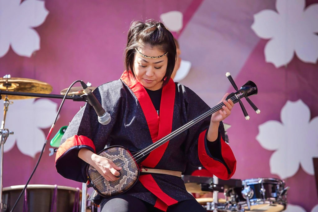 A woman dressed in traditional Japanese clothing plays an Okinawan lute, or sanshin